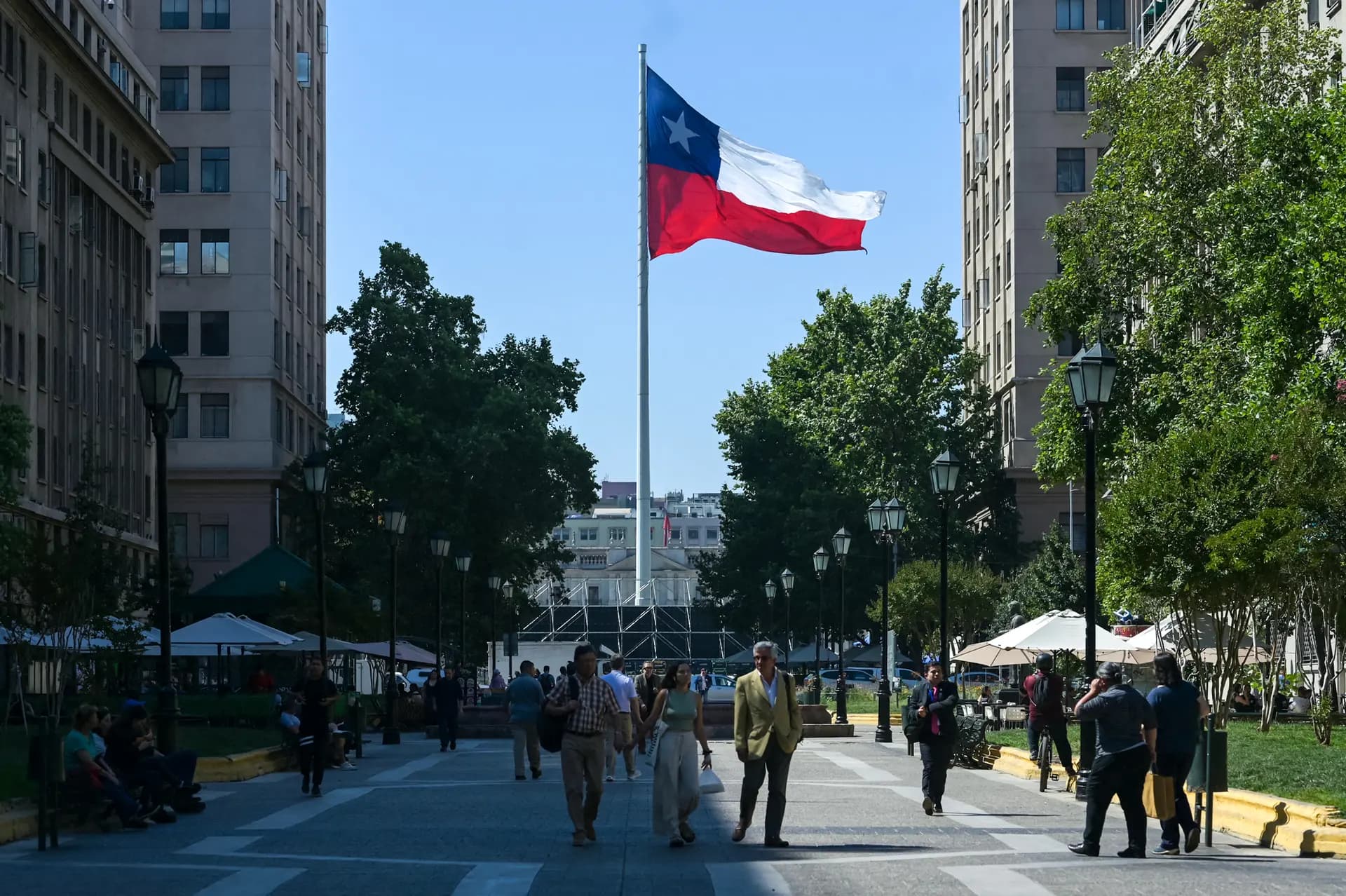 Varias personas pasan junto a una bandera chilena que ondea frente al Palacio Presidencial de La Moneda, en Santiago de Chile, el 9 de diciembre de 2025. (Eitan Abramovich/AFP vía Getty Images).