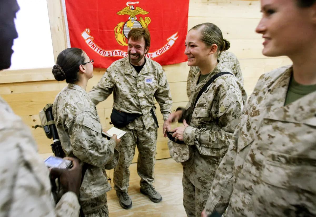 Marines y marineros estadounidenses del Equipo de Combate Regimental 7, con sede en California, se reúnen con la estrella de cine de acción Chuck Norris en la base aérea de Al Asad, en la provincia de Al Anbar, al oeste de Bagdad, el 31 de octubre de 2006. (IM GOODWIN/USMC/AFP vía Getty Images)