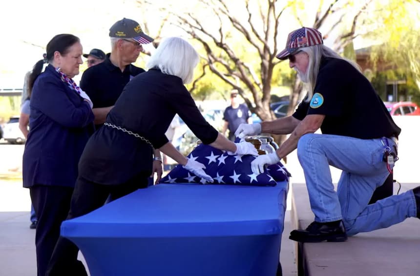 Un voluntario coloca banderas dobladas junto a 15 urnas con cenizas durante un servicio de entierro en el Cementerio Nacional Conmemorativo de Arizona, en Phoenix, el 18 de marzo de 2026. (Allan Stein/The Epoch Times)