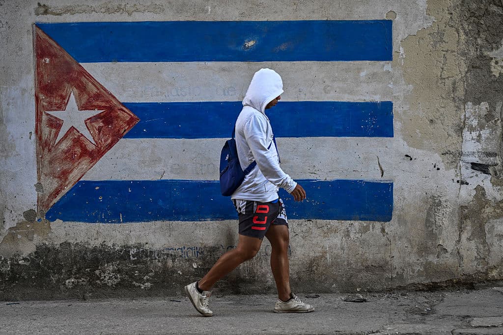 Un hombre pasa junto a un muro pintado con la bandera cubana en una calle de La Habana durante un apagón nacional el 22 de marzo de 2026. El Ministerio de Energía informó que el apagón afectó a toda la isla de Cuba el 21 de marzo, siendo el segundo apagón nacional en menos de una semana, mientras la red eléctrica sufre las consecuencias del bloqueo petrolero estadounidense. (Foto de YAMIL LAGE / AFP vía Getty Images)