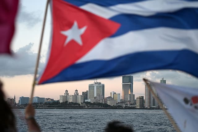 Un activista ondea una bandera cubana a bordo del buque Maguro —rebautizado simbólicamente como "Granma 2.0" en homenaje al yate utilizado por la guerrilla de Fidel Castro para lanzar su revolución en 1956— a su llegada desde México con ayuda humanitaria como parte del convoy Nuestra América, atracando en el puerto de La Habana el 24 de marzo de 2026. El primer barco de una flotilla que transportaba suministros médicos, alimentos y paneles solares llegó a Cuba el 24 de marzo de 2026 para ayudar a la isla, cuya crisis energética se agrava por el bloqueo estadounidense del combustible. El barco camaronero Maguro atracó en La Habana tres días más tarde de lo previsto; otros dos barcos debían llegar después. (Foto de YURI CORTEZ / AFP vía Getty Images)