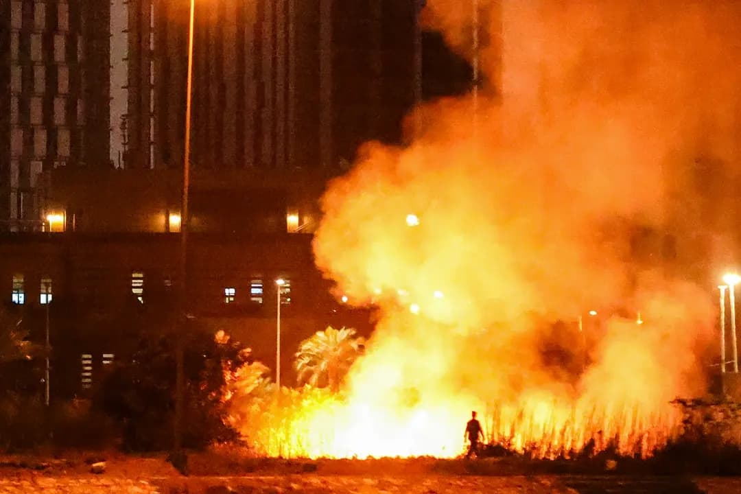 Una persona camina cerca de un incendio que arde fuera del recinto de la embajada de EE. UU. tras un ataque con drones y cohetes en la fortificada Zona Verde de Bagdad, Irak, el 17 de marzo de 2026. (Ahmad Al-Rubaye/AFP vía Getty Images)