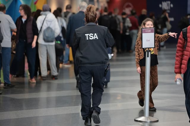 Un agente de la TSA pasa junto a los viajeros que esperan en fila para pasar el control de seguridad en la Terminal 8 del Aeropuerto Internacional John F. Kennedy el 27 de marzo de 2026 en Nueva York, Nueva York. (Michael M. Santiago/Getty Images)