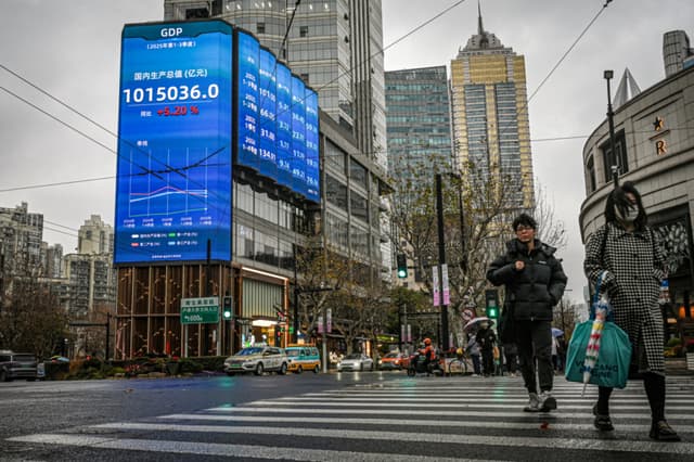 Personas caminan frente a una pantalla que muestra las cifras del producto interno bruto en una calle de Shanghái el 19 de enero de 2026. (Jade Gao/AFP vía Getty Images)