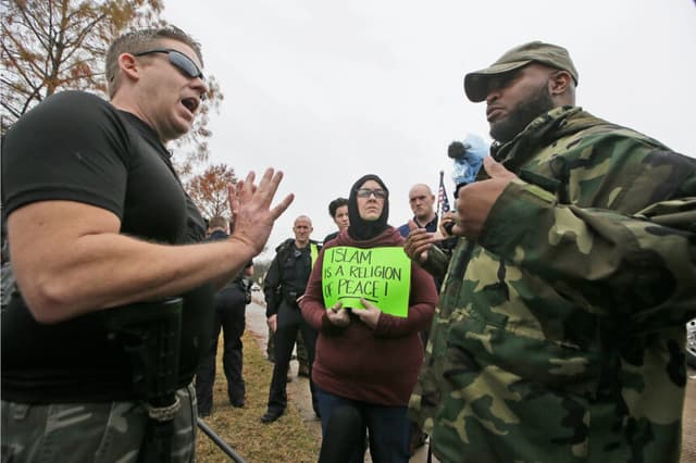 El manifestante David Wright (izq.) habla con el contramanifestante Vincent Simon, un musulmán, mientras Melissa Yassini sostiene un cartel frente a una mezquita en Richardson, Texas, el 12 de diciembre de 2015. (Foto LM Otero/AP)