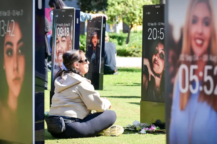 Padres afligidos contemplan las imágenes de sus hijos fallecidos expuestas en el Lost Screen Memorial, una instalación artística de teléfonos inteligentes a gran escala que muestra a 50 niños que perdieron la vida a causa de daños online, en Los Ángeles, el 13 de febrero de 2026. (Frederic J. Brown/AFP vía Getty Images)