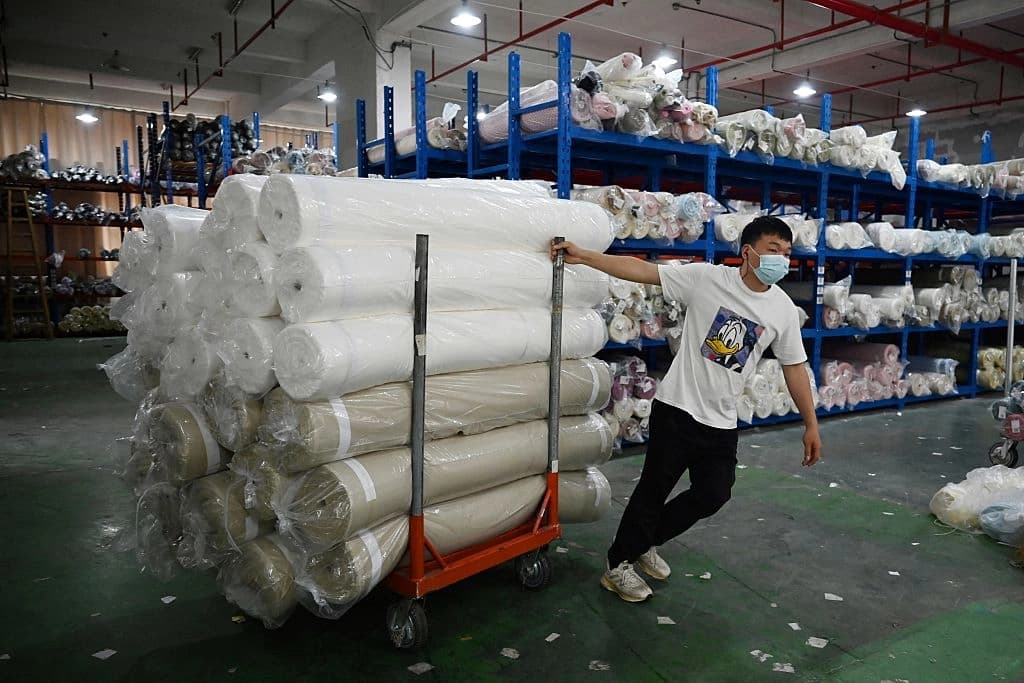 Un trabajador transporta rollos de tela tras descargarlos en un almacén de un polígono industrial textil en Shaoxing, en la provincia oriental china de Zhejiang, el 9 de mayo de 2025. Greg Baker/AFP vía Getty Images