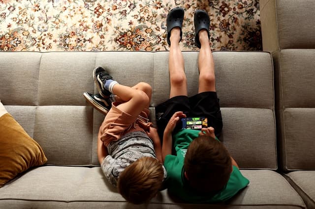 En esta ilustración fotográfica, unos niños pequeños sostienen un iPhone mientras utilizan la plataforma de juegos en línea Roblox el 19 de noviembre de 2025 en Auckland, Nueva Zelanda. (Ilustración fotográfica de Getty Images)