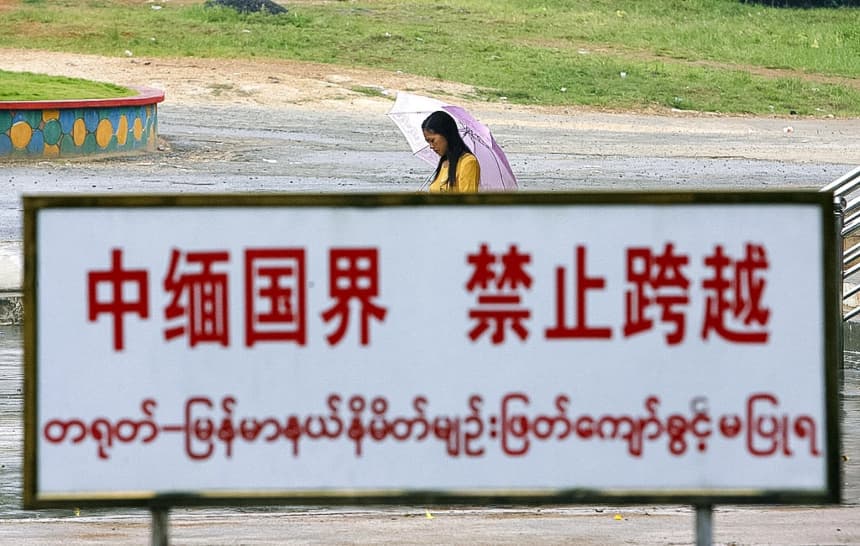 Una mujer birmana camina detrás de una señal de advertencia a lo largo de la línea fronteriza en Wanding, ciudad fronteriza entre China y Birmania, en la provincia sudoccidental de Yunnan, China, el 27 de septiembre de 2007. (STR/AFP vía Getty Images)