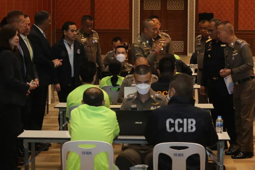 Policías hablan con sospechosos, vestidos con camisetas verde claro y sentados de espaldas a la cámara a la izquierda, en la Oficina de Investigación de Delitos Cibernéticos de Bangkok, el 22 de marzo de 2023. (Oficina de Investigación de Delitos Cibernéticos de Tailandia vía AP)