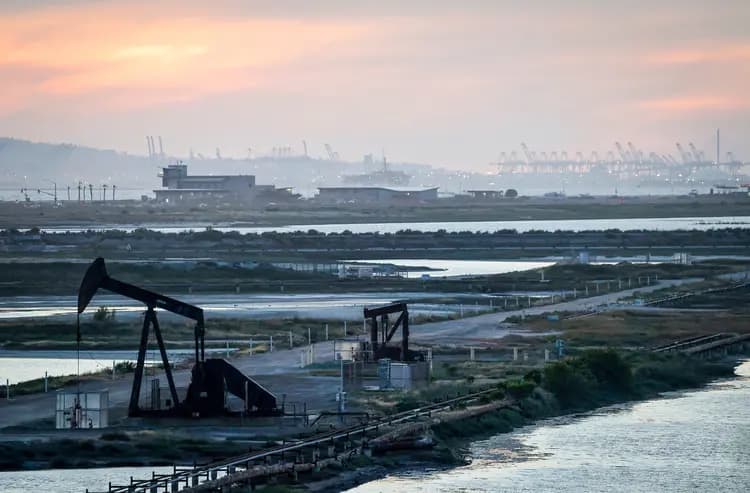 Una bomba de extracción permanece inactiva en el yacimiento petrolífero de Huntington Beach, con grúas portuarias visibles en la distancia, en Huntington Beach, California, el 23 de abril de 2026. Estados Unidos se beneficia no solo del suministro nacional, sino también de importantes importaciones procedentes de Canadá. (Mario Tama/Getty Images)