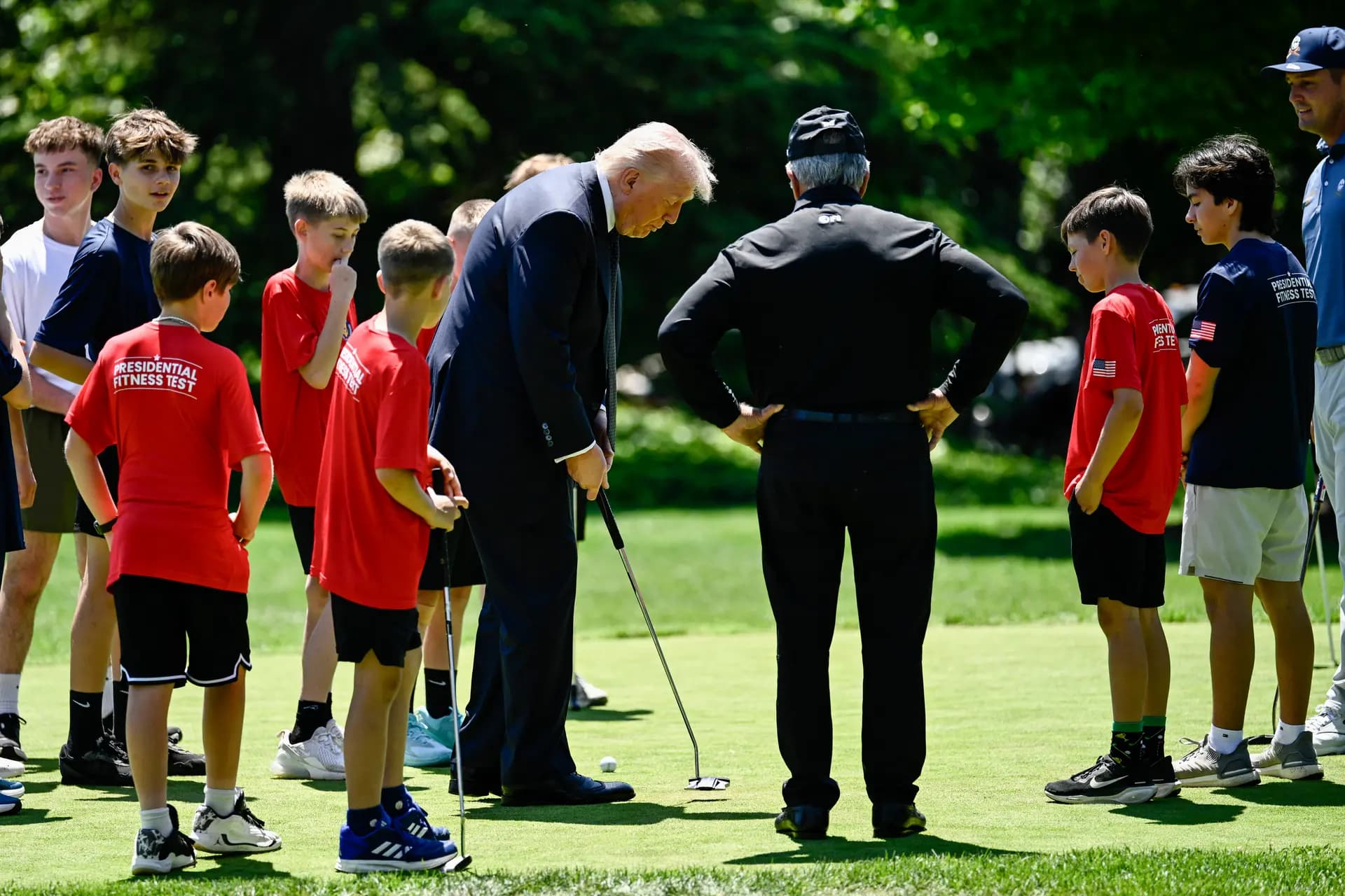 El presidente Donald Trump realiza un golpe de putt mientras el golfista estadounidense Bryson DeChambeau (a la derecha), el golfista sudafricano retirado Gary Player (en el centro) y varios estudiantes deportistas observan desde el green del Jardín Sur de la Casa Blanca, tras la firma por parte de Trump de una proclamación para reactivar el "Presidential Fitness Test Award", un programa competitivo de aptitud física en el ámbito escolar, en Washington, el 5 de mayo de 2026. (Kent Nishimura/AFP vía Getty Images).