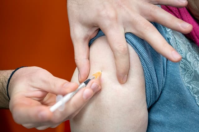 Primer plano de un farmacéutico administrando una inyección de la vacuna contra la COVID-19 en el brazo de una persona mayor con una jeringuilla en una farmacia de Saint-Julien-l'Ars, cerca de Poitiers, en el departamento de Vienne (Francia), el 19 de diciembre de 2025. (Jean-François FORT / Hans Lucas / AFP vía Getty Images)
