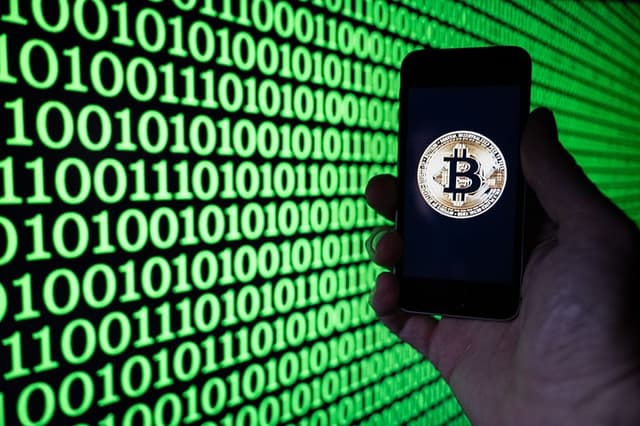 Esta fotografía ilustrativa muestra a un hombre sosteniendo un teléfono en el que se ve el logotipo de Bitcoin, en Mulhouse, el 5 de diciembre de 2025. (SEBASTIEN BOZON / AFP vía Getty Images)
