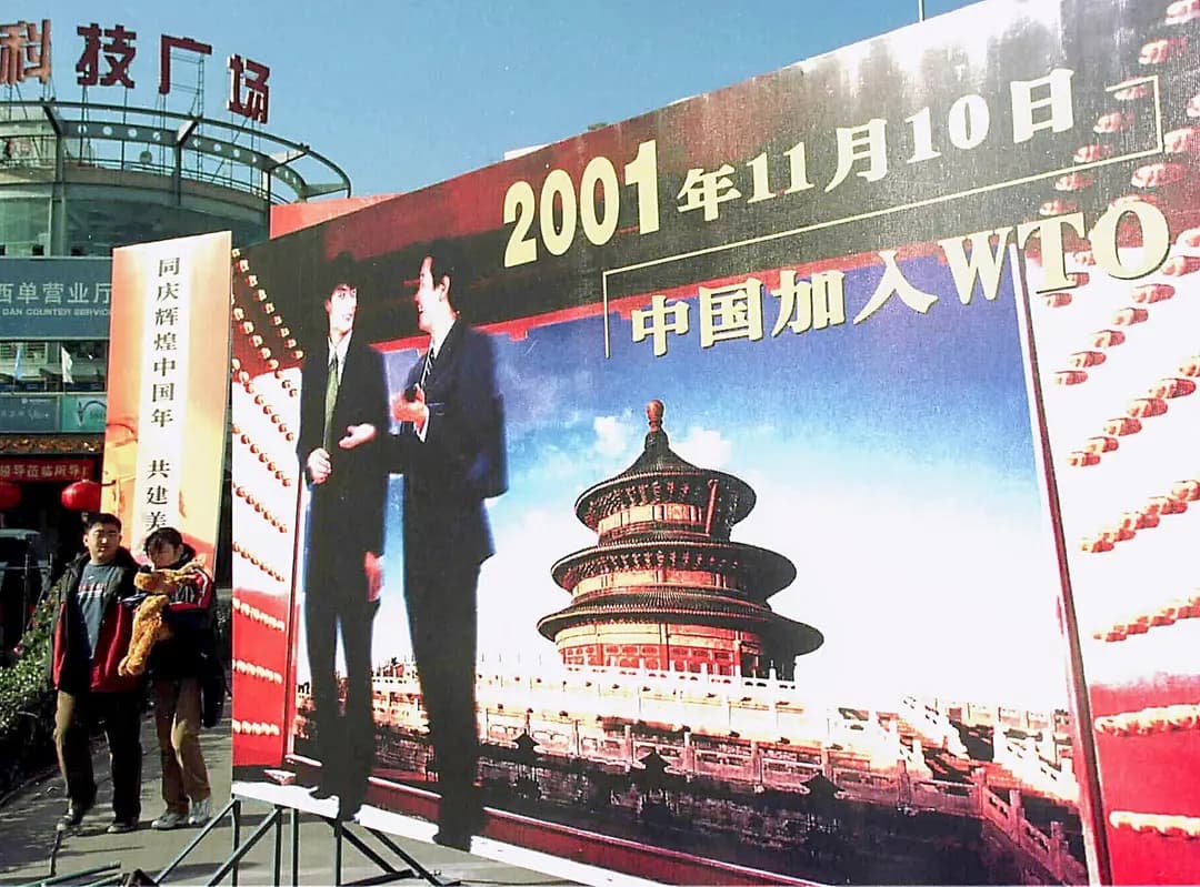 La gente pasa junto a una valla publicitaria que celebra la entrada de China a la Organización Mundial del Comercio en 2001, en Beijing, el 5 de enero de 2002. El nivel de vida mejoró en China a medida que el Partido Comunista Chino abrió el país al capital, la tecnología y los mercados occidentales. (AFP vía Getty Images)
