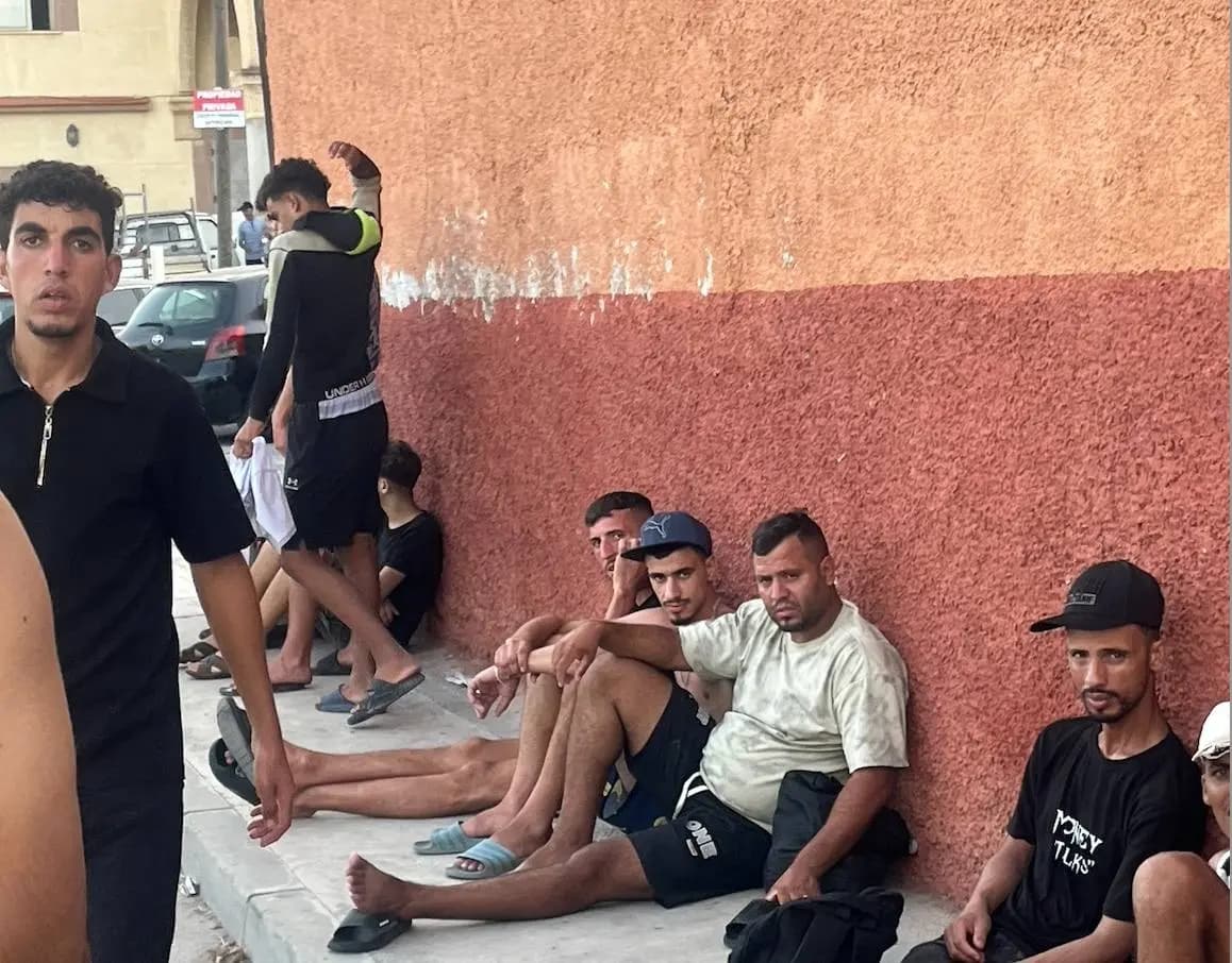 Migrantes marroquíes descansan tras llegar desde Marruecos junto a una pared en una acera de Ceuta, el 31 de julio de 2026. (Etienne Fauhaire/The Epoch Times)