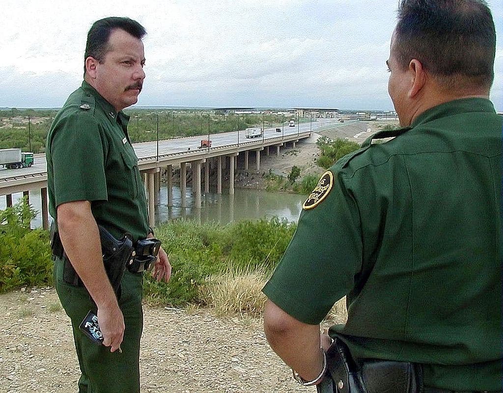 <em>Agentes estadounidenses de la patrulla de frontera vigilan uno de los puentes del paso fronterizo entre Laredo (EE. UU.) y Nuevo Laredo (México), el 26 de agosto de 2000. Los indocumentados que intentan ingresar a Estados Unidos se enfrentan al aumento en la vigilancia y a la tarifa de los traficantes que los cruzan. (Raul Llamas/AFP via Getty Images)</em>