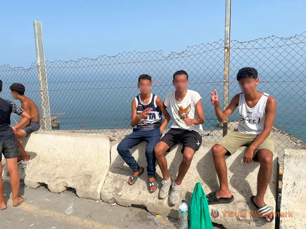 <em>Tres jóvenes marroquíes, Nazir (14), Wassim (15) y Yassine (15), están sentados junto a una valla con vistas al mar en Ceuta, España, el 1 de agosto de 2026. (Etienne Fauchaire/The Epoch Times).</em>