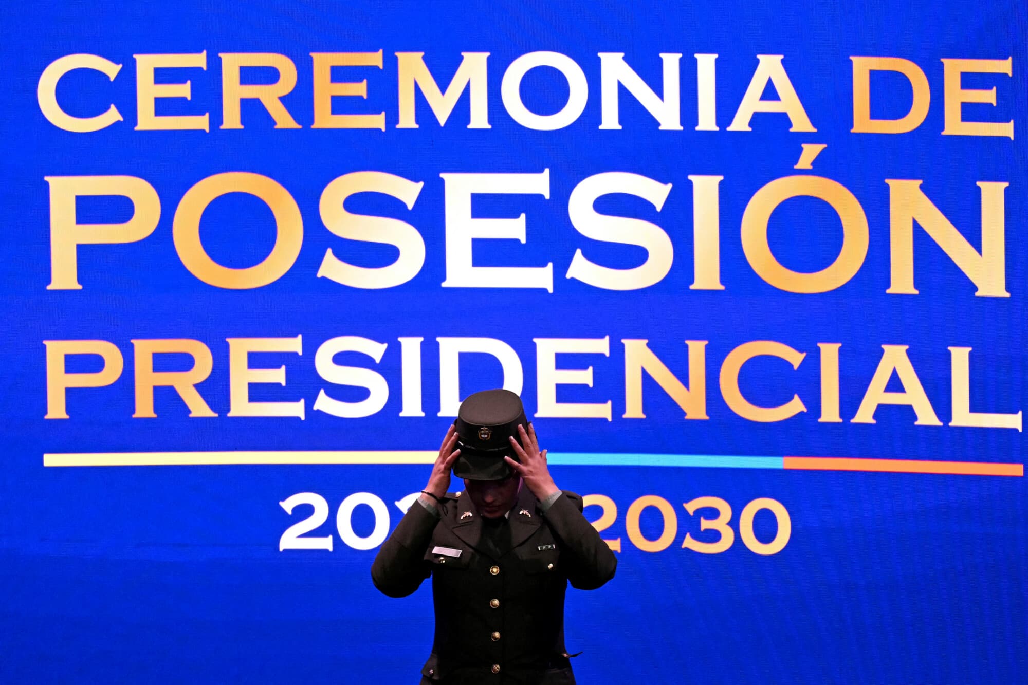 Una agente de seguridad se ajusta el sombrero en el escenario, frente a un telón en el que se lee "Ceremonia de toma de posesión presidencial 2026-2030", antes de que el presidente electo de Colombia, Abelardo de la Espriella, preste juramento durante su ceremonia de toma de posesión en la Universidad Santiago de Cali, en Cali, Colombia, el 7 de agosto de 2026. (Luis ACOSTA / AFP vía Getty Images)<br/><br/>