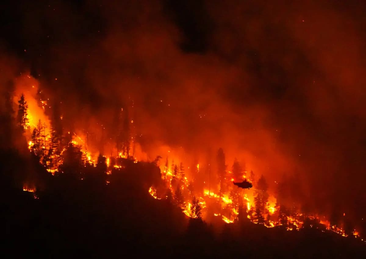 Un helicóptero que realiza operaciones nocturnas se prepara para lanzar agua sobre el incendio forestal de Quilpituk Creek, que arde en el lado oeste del lago Okanagan, cerca de Fintry, Columbia Británica, el 3 de agosto de 2026. (The Canadian Press/Darryl Dyck)