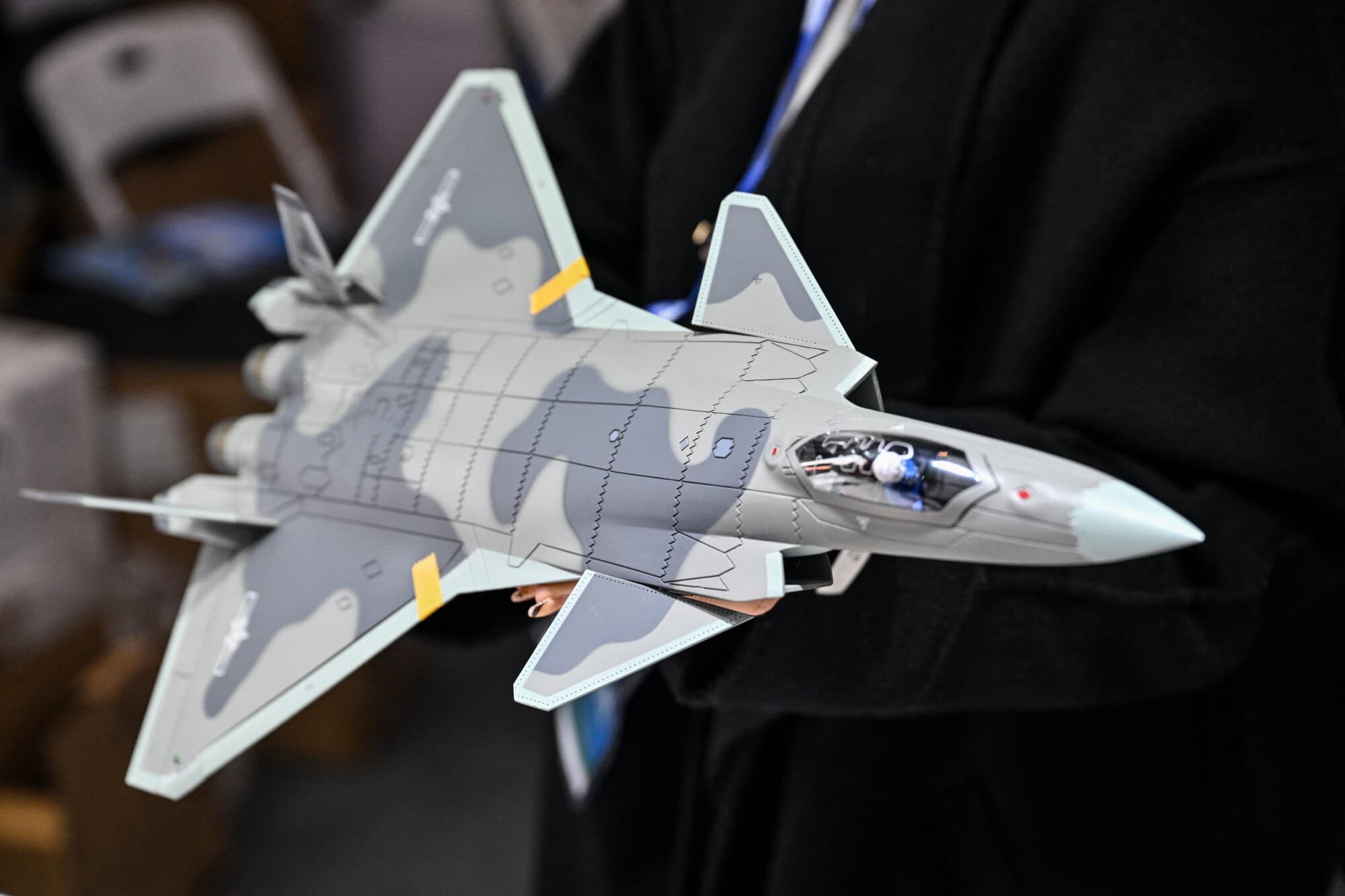 Una mujer sostiene una réplica a escala del caza furtivo Chengdu J-20, de fabricación china, en un stand durante la feria Aero Asia 2025 en Zhuhai, en la provincia de Guangdong, al sur de China, el 28 de noviembre de 2025. (Héctor RETAMAL / AFP vía Getty Images)