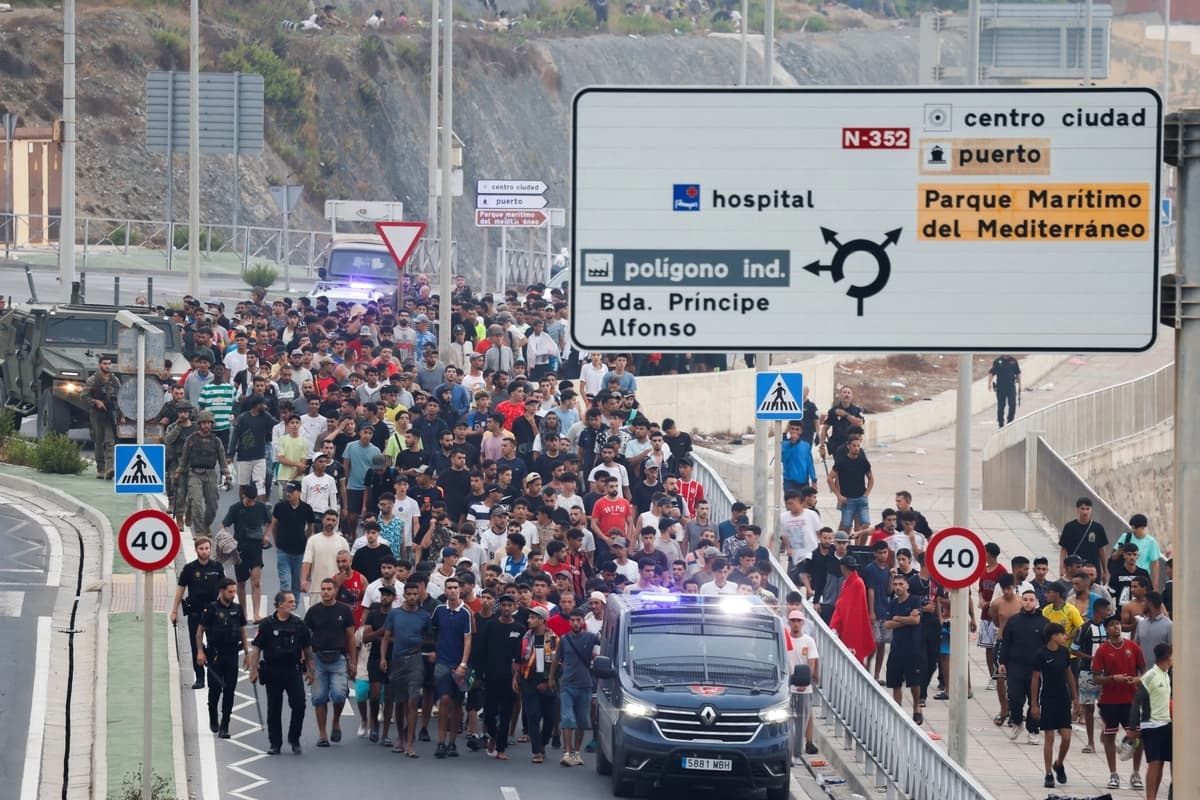 Agentes de policía y soldados escoltan a un numeroso grupo de migrantes hacia la frontera para sacarlos de España, tras los cruces masivos de migrantes a pie y por mar desde Marruecos hacia Ceuta el 1 de agosto de 2026. (Reuters/Jon Nazca)
