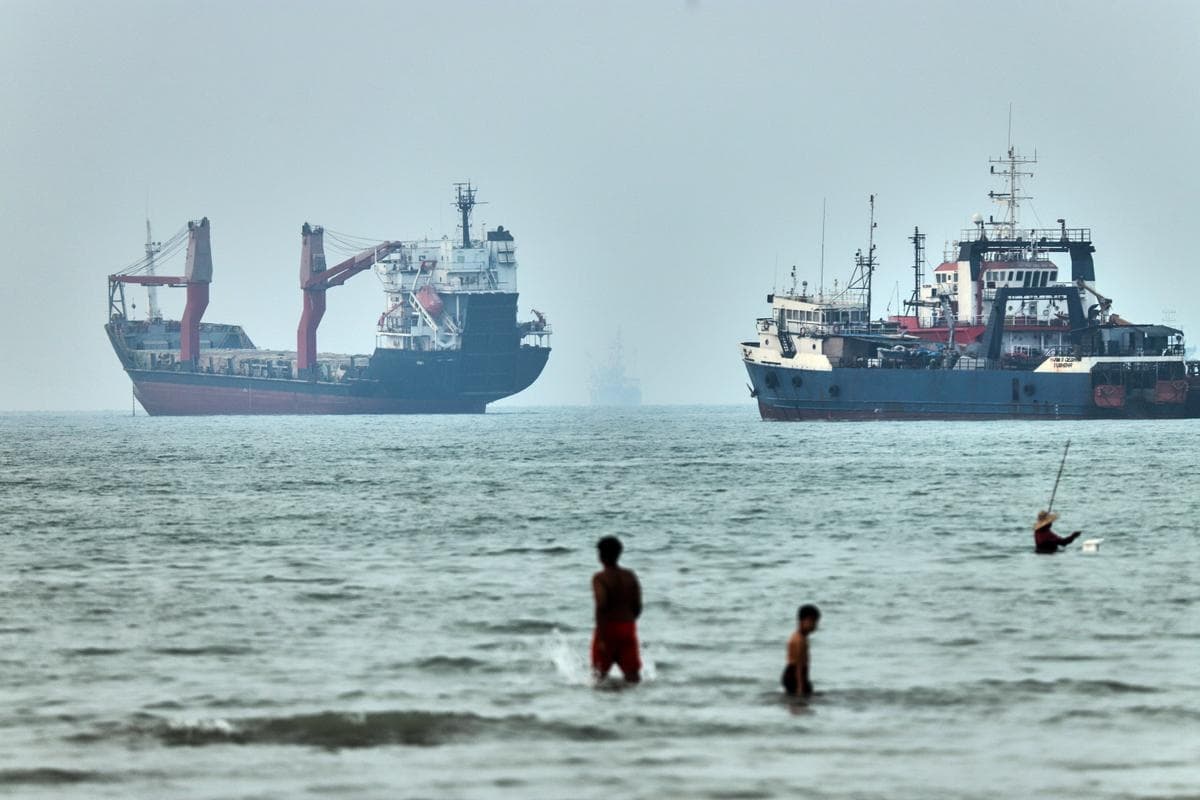 Personas vadean el agua con buques de carga anclados al fondo, en el Estrecho de Ormuz, frente a Bandar Abbas, Irán, el 30 de junio de 2026. (Amirhosein Khorgooi/ISNA vía AP)