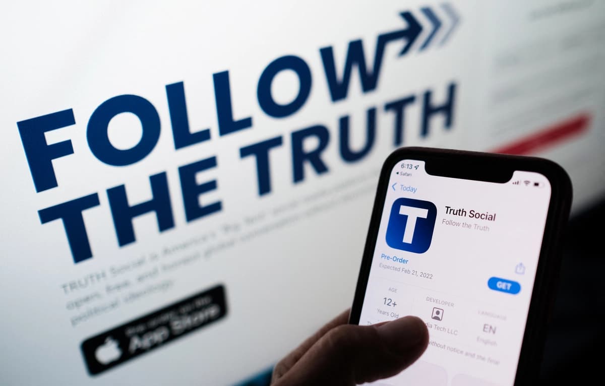 Esta foto ilustrativa muestra a una persona buscando Truth Social en la tienda de aplicaciones de su teléfono inteligente, con su sitio web en la pantalla de una computadora al fondo, en Los Ángeles el 20 de octubre de 2021. (Chris Delmas/AFP vía Getty Images).