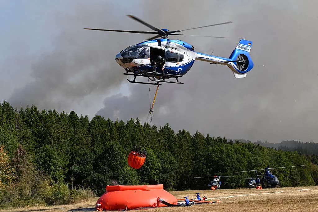 <em>Helicópteros policiales cargan agua para combatir un incendio forestal en Hürtgenwald, al oeste de Alemania, el 14 de agosto de 2026. Alrededor de 1800 personas tuvieron que abandonar sus hogares en el oeste de Alemania durante la noche debido a la propagación de un incendio forestal en las cercanías, según informaron las autoridades. Se desplegaron helicópteros y equipo militar para ayudar a combatir las llamas. (Roberto Pfeil/AFP vía Getty Images).</em>