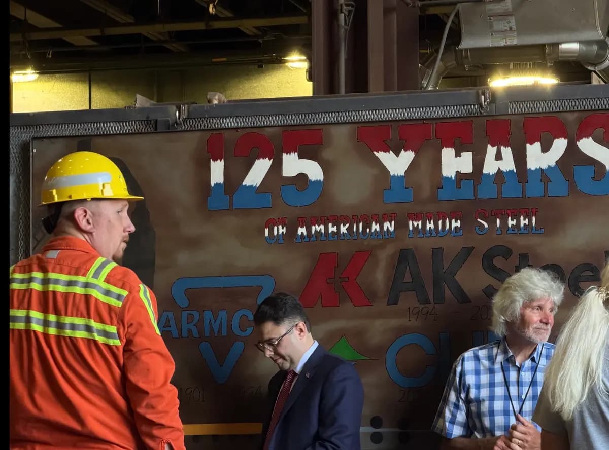 Un trabajador siderúrgico se encuentra frente a un cartel que celebra los "125 años de acero fabricado en Estados Unidos", el cual muestra los logotipos de las tres empresas que fueron propietarias de la planta en Middletown, Ohio, donde el vicepresidente JD Vance tenía previsto hablar el 21 de agosto de 2026. (Janice Hisle/The Epoch Times)