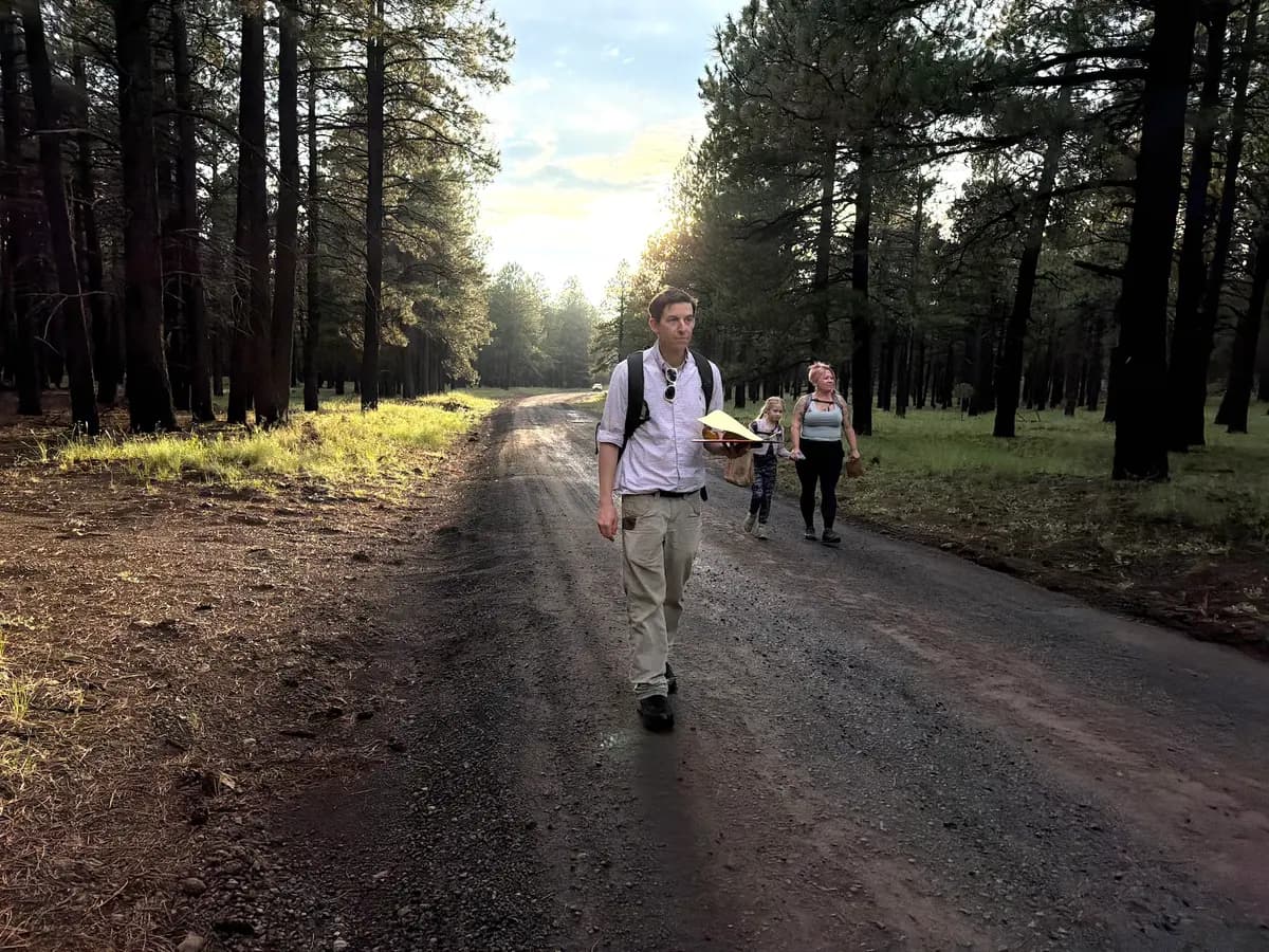 <em>El director ejecutivo de la Sociedad Micológica de Arizona, Mike Dechter, camina por un camino forestal seguido por las recolectoras de setas aficionadas Michelle Lindsay (derecha) y su hija Jovie, de 7 años, el 14 de agosto de 2026. (Allan Stein/The Epoch Times).</em>