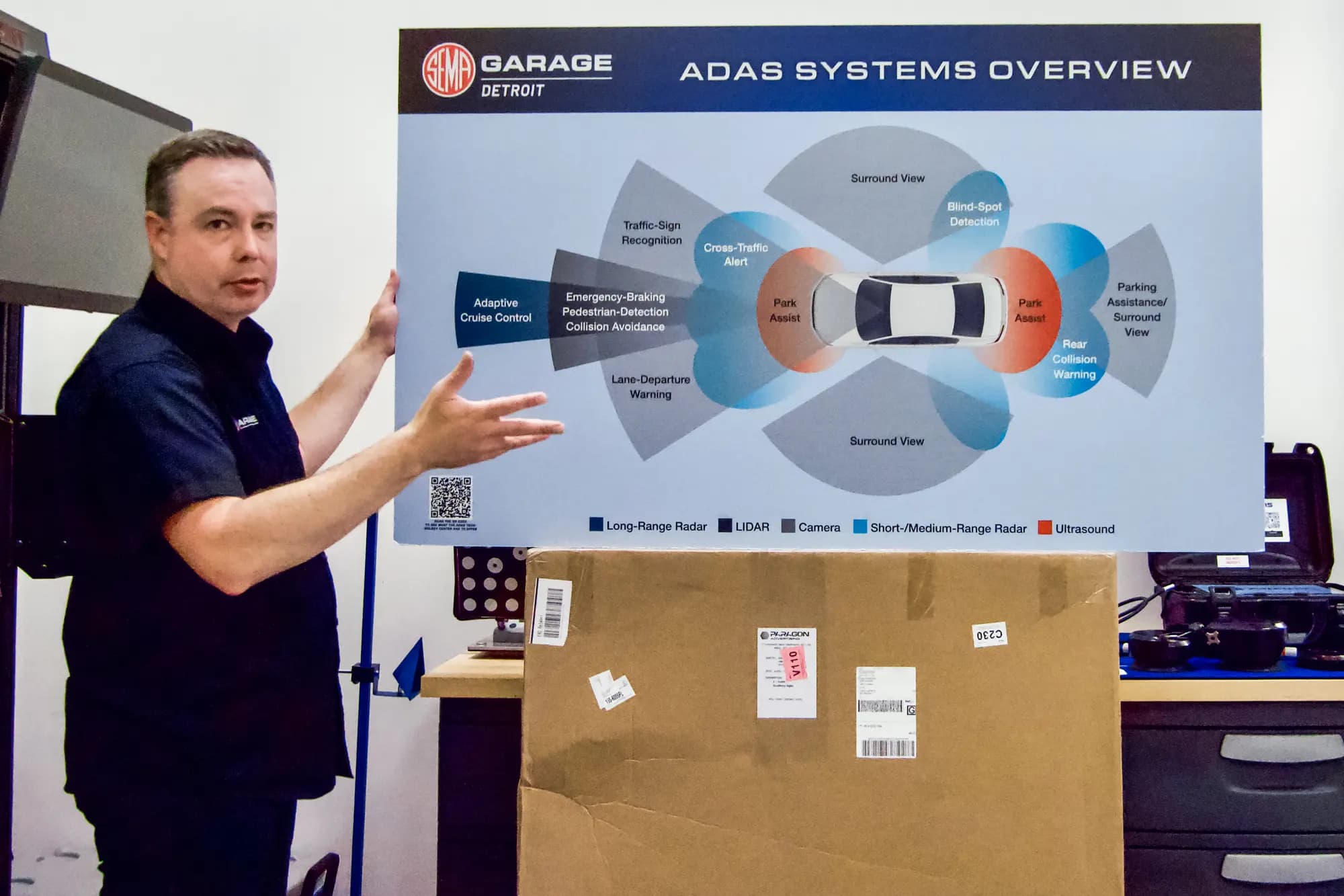 <em>Ben Kaminsky, gerente general del Detroit Garage de SEMA, muestra un cartel que ilustra los sensores utilizados en los sistemas automáticos de asistencia al conductor de los vehículos en las instalaciones de la organización en Plymouth, Michigan, el 28 de julio de 2026. (Travis Gillmore/The Epoch Times).</em>