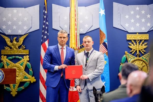 El secretario de Guerra Pete Hegseth (izquierda) posa para una foto con el cabo de la Infantería de Marina Michael Gretzon y su perra Shylah durante un evento en honor a los marines que prestaban servicio durante el atentado de Abbey Gate de 2021, en el Pentágono en Arlington, Virginia, el 26 de agosto de 2026. (Andrew Harnik/Getty Images)