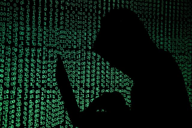 En esta ilustración, un hombre encapuchado sostiene una computadora portátil mientras se proyecta código cibernético sobre ella. (Kacper Pempel/Reuters).