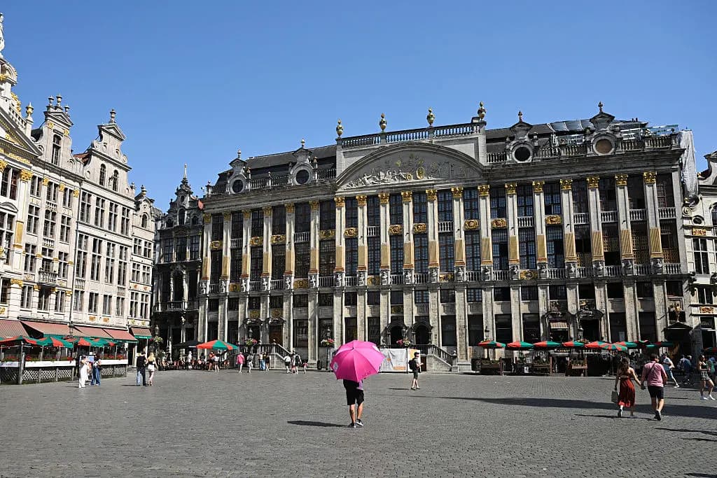 Un guía turístico se protege con un paraguas mientras camina por la Grand-Place durante una ola de calor en Bruselas el 24 de junio de 2026. (Nicolas Tucate/AFP vía Getty Images).
