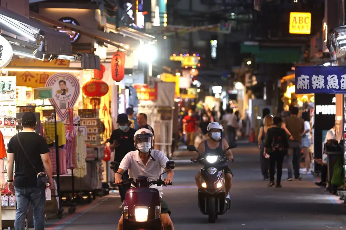 Las personas usan cubrebocas mientras conducen sus motocicletas, mientras otras compran en un mercado nocturno en Taipéi, Taiwán, el 15 de mayo de 2021. (Ann Wang/Reuters)
