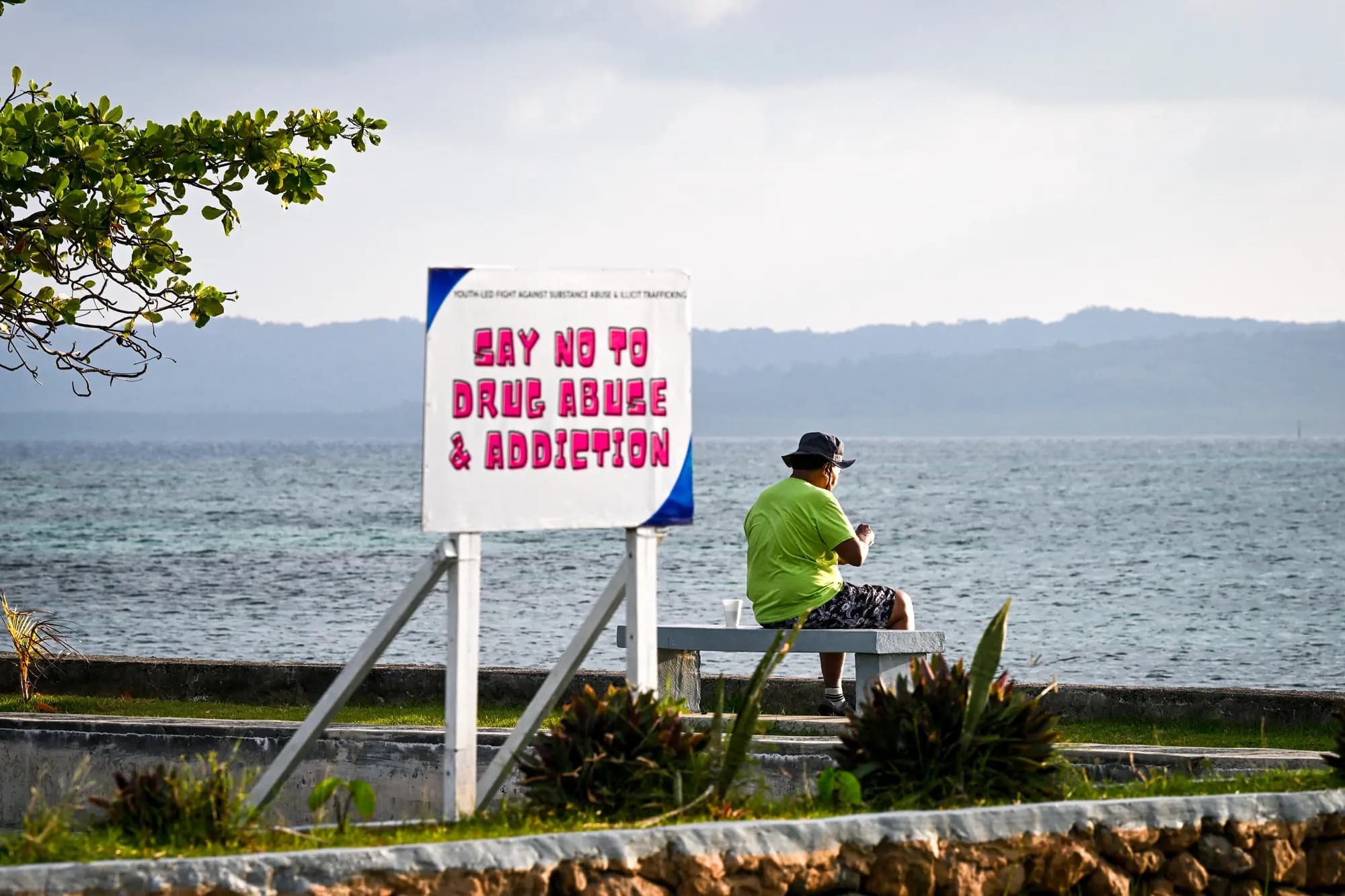 <em>Un hombre se sienta cerca de un cartel colocado en una playa de Koror, Palaos, el 31 de agosto de 2026. El cartel refleja los esfuerzos del país por frenar el creciente problema de las drogas. (Saeed Khan/AFP vía Getty Images).</em>