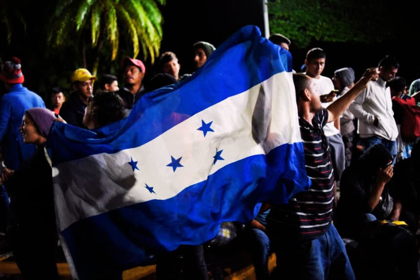 Migrantes hondureños que se dirigen en caravana hacia Estados Unidos sostienen una bandera nacional de Honduras mientras se reúnen en el parque central de Ciudad Tecún Umán, Guatemala, en la frontera con México, el 19 de octubre de 2018. (JOHAN ORDONEZ/AFP vía Getty Images)