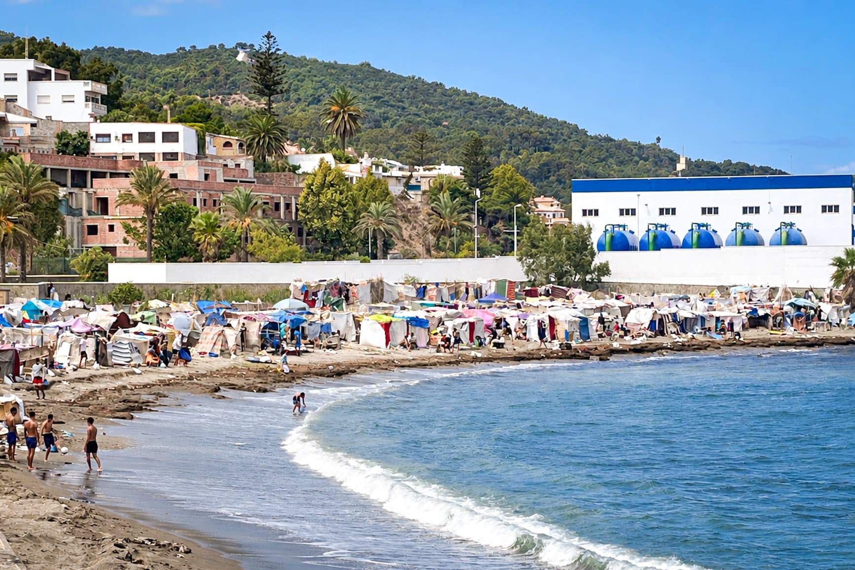 (Arriba) Migrantes ilegales se sientan junto a las grandes tiendas del nuevo campamento de recepción Los Rosales, en Ceuta, España, el 12 de septiembre de 2026. Más de 800 personas fueron trasladadas allí desde el campamento Loma Colmenar. (Abajo) Un denso campamento de tiendas y lonas cubre la playa de Benítez, en Ceuta, el 19 de septiembre de 2026. (Antonio Sempere/AFP vía Getty Images; Etienne Fauchaire/The Epoch Times).
