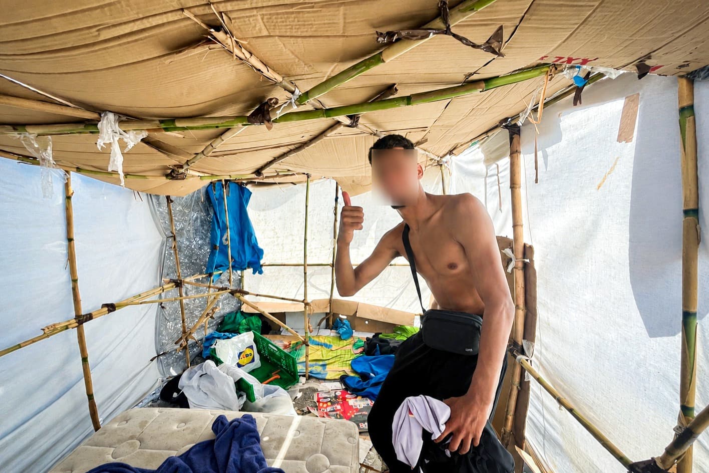Cañas, cartón y láminas de plástico forman un refugio improvisado sobre un colchón y algunas pertenencias dispersas en la playa de Benítez, en Ceuta (España), el 19 de septiembre de 2026. (El rostro de la persona en esta imagen ha sido difuminado a petición del propio individuo). (Etienne Fauchaire/The Epoch Times).