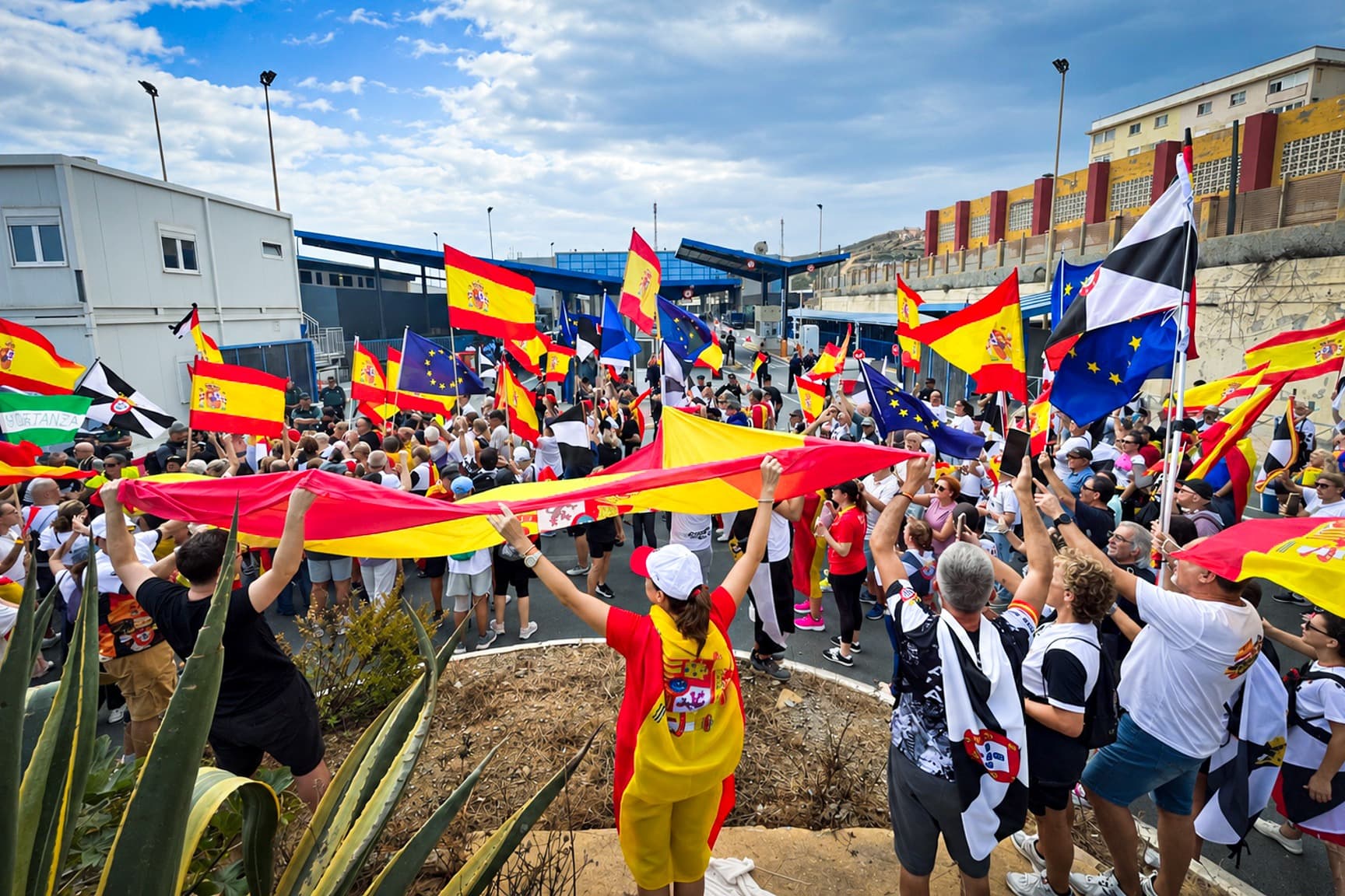 (Arriba) Residentes de Ceuta ondean banderas españolas y locales mientras marchan hacia la frontera de Tarajal, en una manifestación organizada por asociaciones vecinales, el 20 de septiembre de 2026. (Abajo) Manifestantes extienden una gran bandera española y ondean banderas de España, Ceuta y la UE frente al puesto fronterizo de Tarajal, al finalizar la marcha. (Etienne Fauchaire/The Epoch Times).