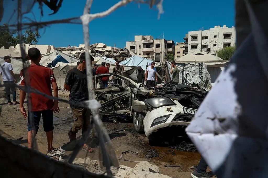 Residentes caminan por una zona dañada junto a un automóvil destruido tras los ataques israelíes en la ciudad de Gaza el 1 de septiembre de 2026. (Eyad Azam/Middle East Images/AFP vía Getty Images)