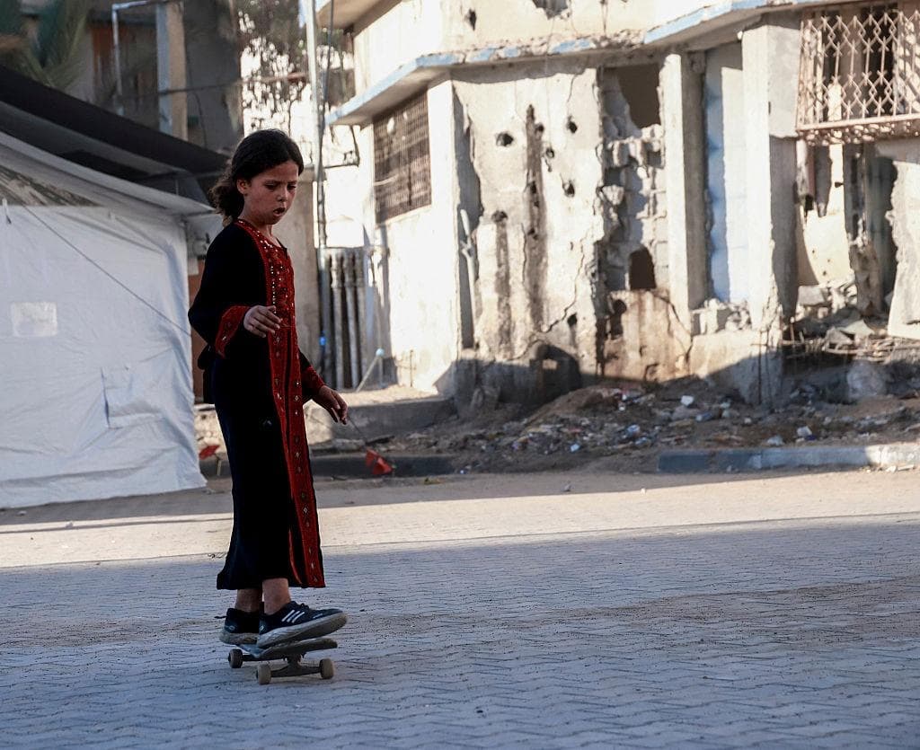 Una niña anda en patineta por una calle pavimentada junto a edificios dañados y una tienda de campaña para desplazados en la Franja de Gaza, el 23 de septiembre de 2026. (Mohammed Abusalama/Middle East Images/AFP vía Getty Images)