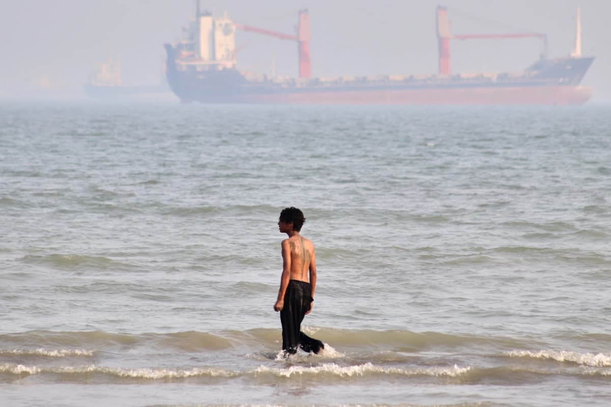 Un niño camina sobre aguas poco profundas mientras buques mercantes permanecen anclados en el estrecho de Ormuz, frente a Bandar Abbas, Irán, el 31 de agosto de 2026. (Razieh Poudat/ISNA vía AP)
