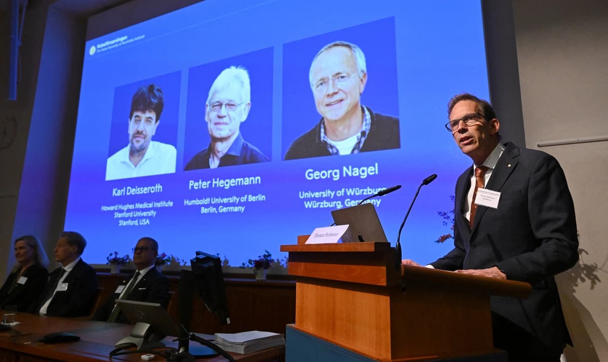 El secretario general del Comité Nobel, Thomas Perlmann (derecha), habla con los medios de comunicación frente a una pantalla que muestra los nombres de los galardonados de este año (izquierda-derecha): Karl Deisseroth, Peter Hegemann y Georg Nagel, durante el anuncio de los ganadores del Premio Nobel de Fisiología o Medicina 2026 en el Instituto Karolinska de Estocolmo, el 5 de octubre de 2026. (Jonathan Nackstrand/AFP vía Getty Images)
