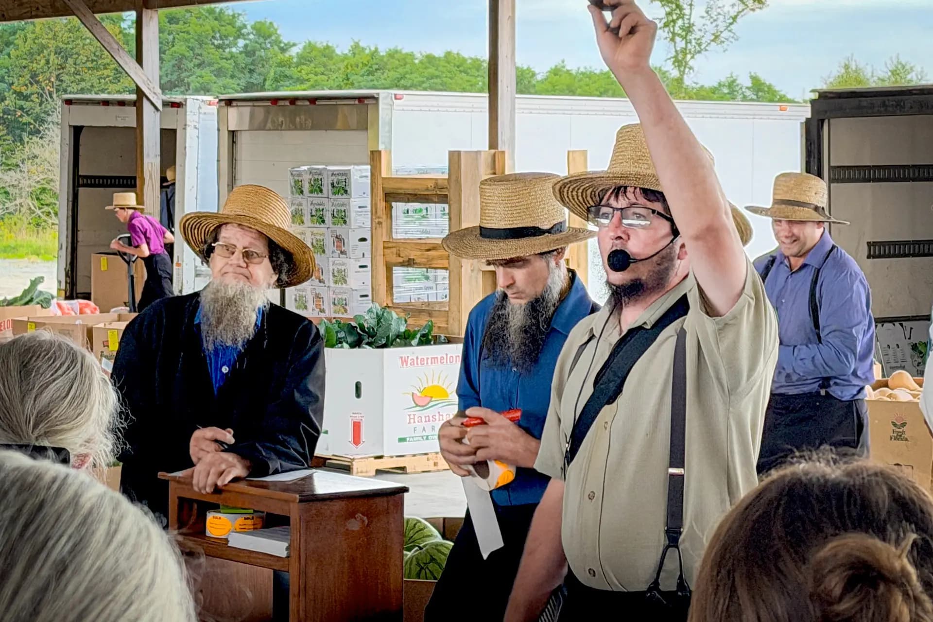 (Arriba) Un subastador amish examina crisantemos a la venta en la subasta de productos agrícolas de Mohawk Valley en Fort Plain, Nueva York, el 18 de septiembre de 2026. (Abajo) Un subastador  una muestra de productos agrícolas. (Allan Stein/The Epoch Times).