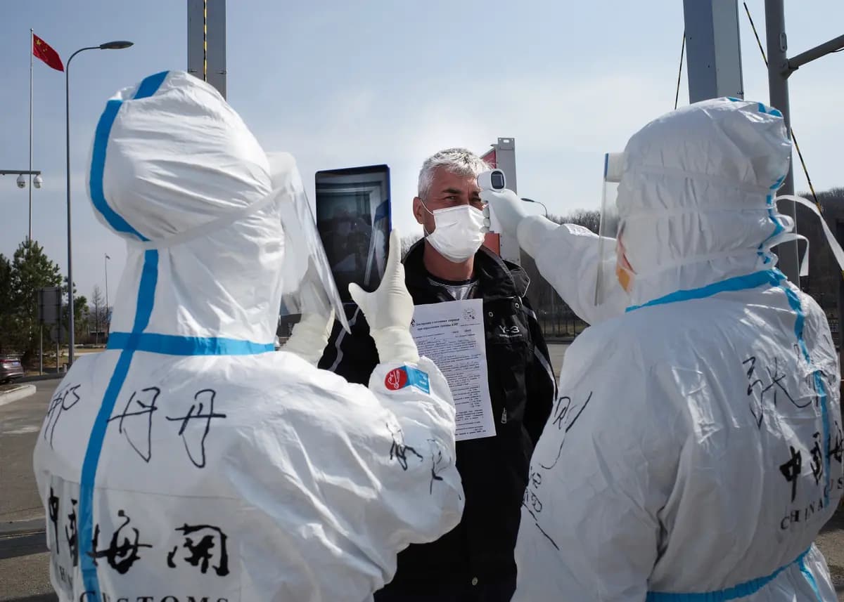 <em>Personal con trajes de protección contra materiales peligrosos toma la temperatura de un conductor en un puesto de control aduanero en la frontera con Rusia en Suifenhe, China, el 1 de mayo de 2020. (STR/AFP vía Getty Images).</em>