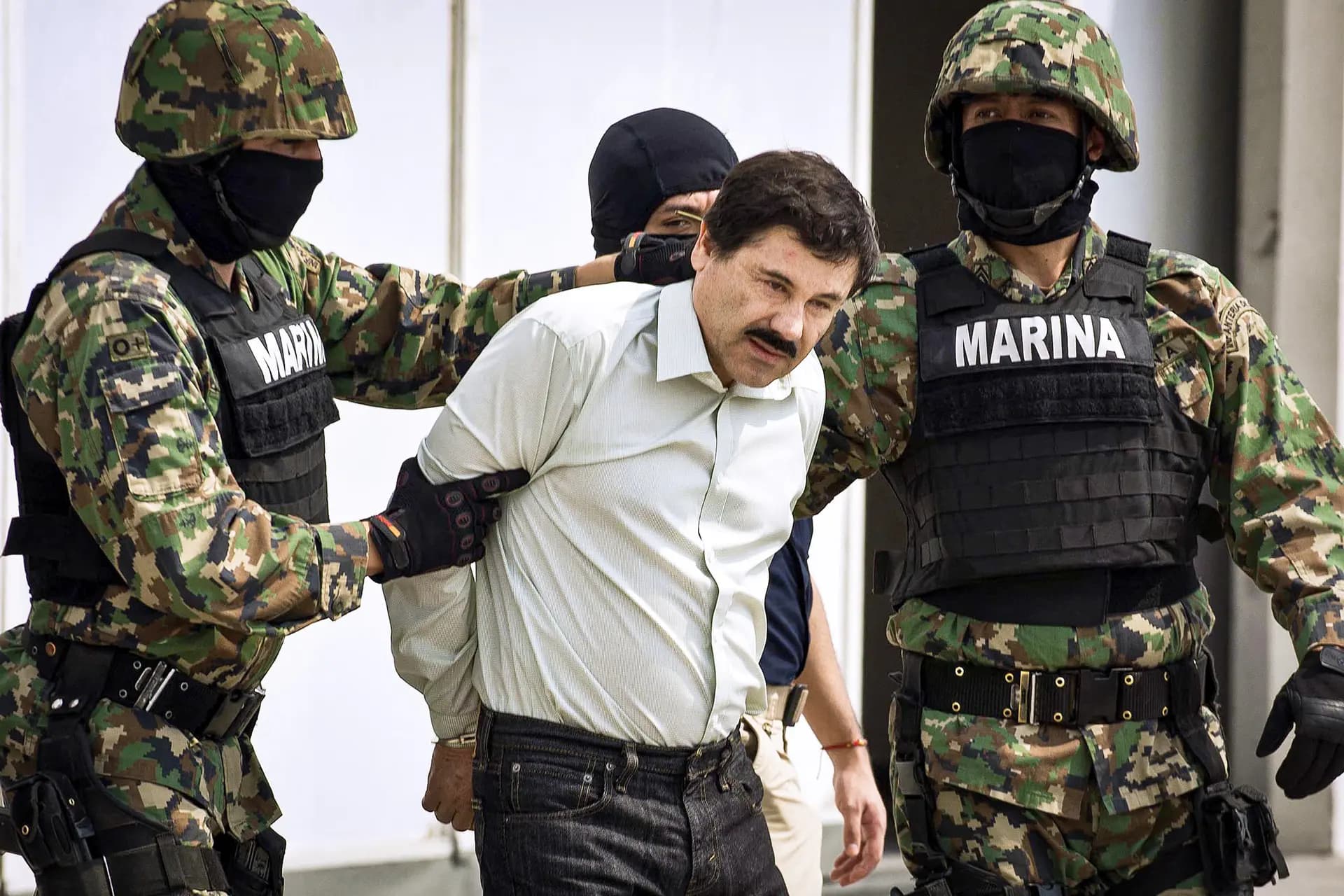 El narcotraficante mexicano Joaquín Archivaldo Guzmán Loera, más conocido como "El Chapo" (C), es escoltado por marines mientras es presentado ante la prensa en Ciudad de México el 22 de febrero de 2014. En 2015, El Chapo se fugó de su celda en una prisión de máxima seguridad cercana a Ciudad de México a través de una elaborada red de túneles. (Ronaldo Schemidt/AFP vía Getty Images)