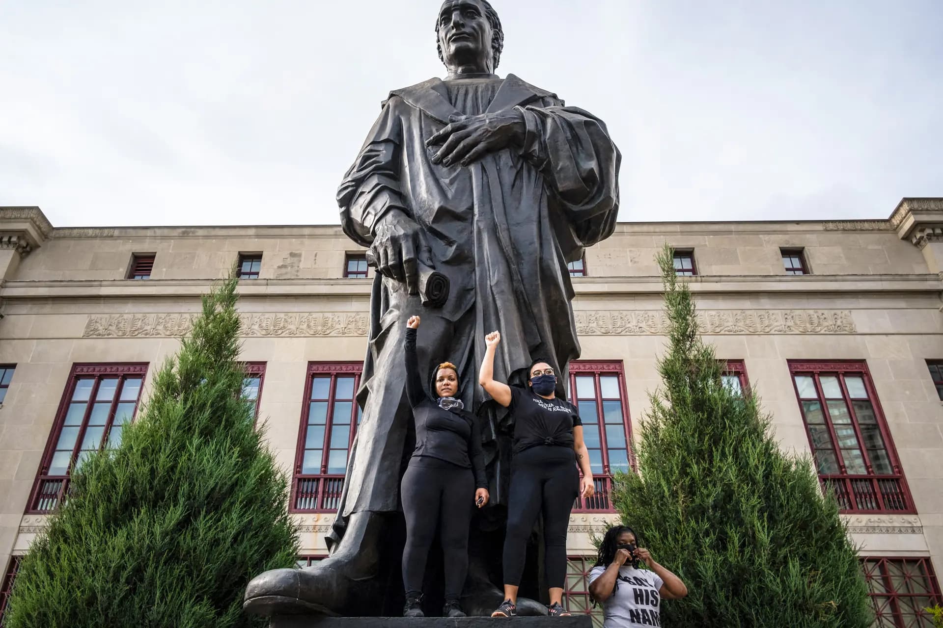 Manifestantes levantan los puños mientras se encuentran al pie de una estatua de Cristóbal Colón frente al ayuntamiento en el centro de Columbus, Ohio, el 27 de junio de 2020, durante una protesta de la Marcha Internacional por las Vidas Negras. (Seth Herald/AFP vía Getty Images).
