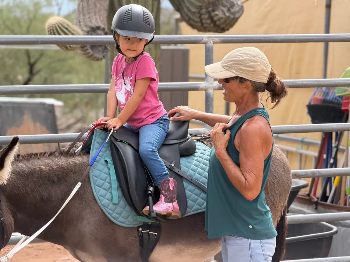 Sophie Rainer, fundadora de Donkeys of the Heart, un programa de terapia asistida con burros en Cave Creek, Arizona, ayuda a Dylan, de 4 años, a mantenerse seguro en la silla de montar con Alfred, un burro de 11 años, el 24 de septiembre de 2026. (Allan Stein/The Epoch Times)